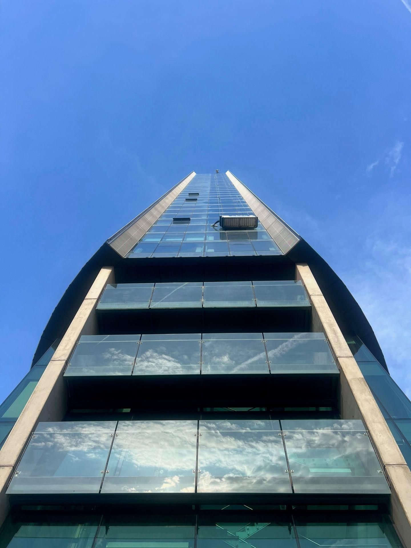 Upward view of a modern high-rise building with glass windows reflecting the blue sky and clouds.